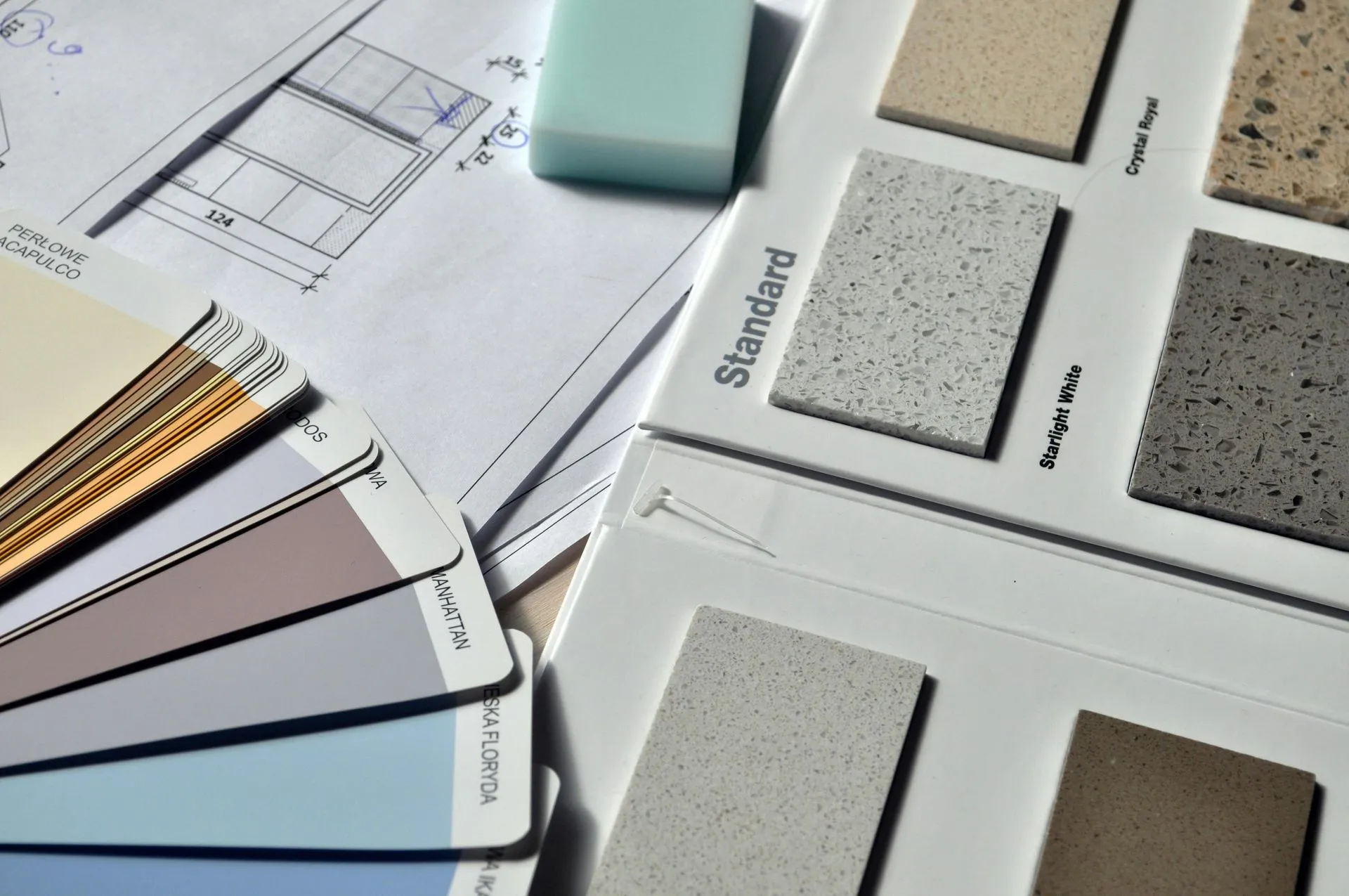 Color swatches, tile samples, and architectural plans on a desk. The design layout includes various textures and hues, suggesting interior design