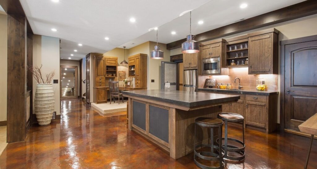 Spacious kitchen with wooden cabinetry, large island with stools, stainless steel appliances, and warm lighting, featuring glossy brown floors.